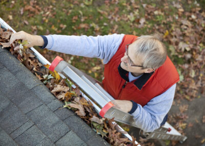 Man up ladder cleaning leafs out of gutter on house